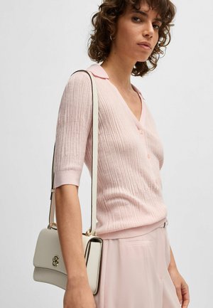 Maglione a coste rosa con scollo a V e maniche corte, abbinato a una borsa bianca con hardware dorato e tracolla.