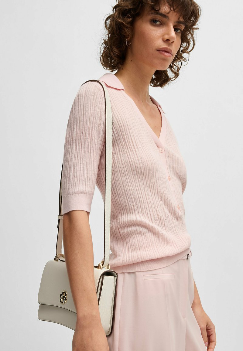 Maglione a coste rosa con scollo a V e maniche corte, abbinato a una borsa bianca con hardware dorato e tracolla.