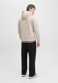 Beige Kapuzenpullover mit lockerer Passform, kombiniert mit schwarzen weiten Hosen. Weicher Stoff mit gerippten Bündchen; ausgestattet mit einer Kängurutasche.