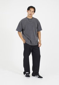 Grå oversized bomulls t-shirt med korta ärmar, avslappnad passform, tillsammans med svarta vida byxor och svarta sneakers med vita ränder.