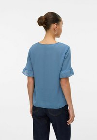 Top blu corto con maniche a sbuffo e scollatura rotonda, caratterizzato da una consistenza liscia, abbinato a jeans scuri.