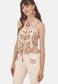 Top sin mangas de patrón multicolor con acentos de encaje y un dobladillo con volantes, combinado con pantalones claros con detalles bordados.