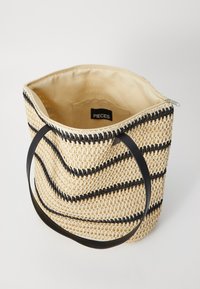 Vevd stråtask med svarte striper, beige innside og kraftige svarte håndtak. Har en glidelås og en merkeetikett inni.