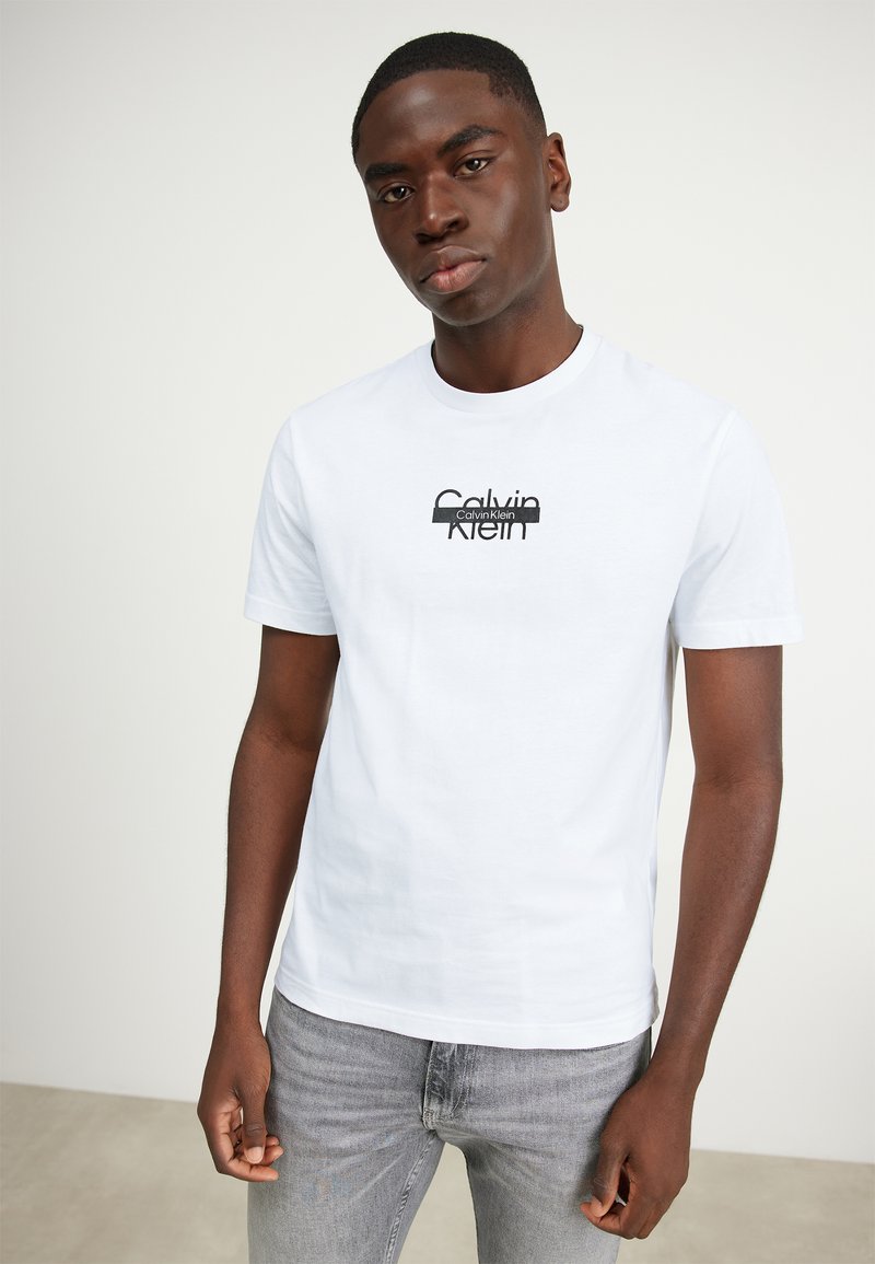 Hvit kortermet bomull T-skjorte med en svart Calvin Klein-logo på brystet. Passformen er standard, med vanlig rund hals.
