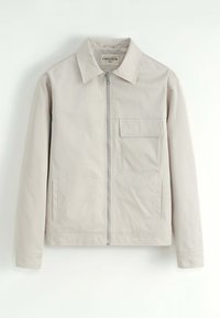 Veste zippée beige clair avec col, poche de poitrine plaquée sur le côté gauche et deux poches verticales sur les côtés, affichée sur fond blanc.