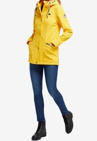 Yellow waterproof jacket with a hood, zipper, two side pockets, and decorative drawstrings. Paired with blue jeans and black lace-up boots.
