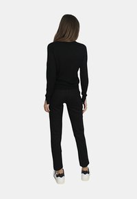 Maglione nero a maglia con maniche lunghe, abbinato a pantaloni neri slim-fit e sneakers bianche spesse con un accento nero.