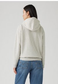 Ljusgrå huvtröja med texturerad yta, med ribbade manschetter och nederkant, kombinerad med högmidjade blå jeans.