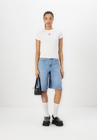 Camiseta blanca de manga corta con un pequeño logo rojo, pantalones cortos de mezclilla azules, zapatos de plataforma negros, calcetines blancos y un bolso negro.