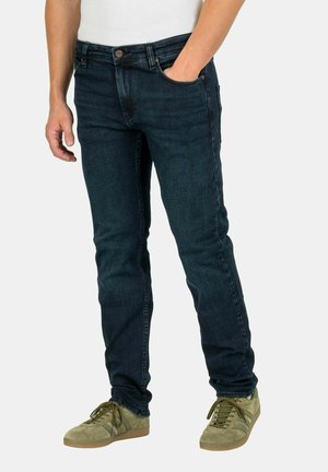 Dunkelblaue Slim-Fit-Jeans aus Denim mit Fronttaschen und Knopfverschluss; kombiniert mit grünen Wildledersneakern.