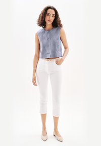 Top in gingham blu con chiusura a bottoni, abbinato a pantaloni cropped bianchi aderenti e scarpe con tacco beige. Design semplice e vestibilità su misura.