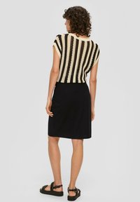 Zwarte rok gecombineerd met een gebreide top met korte mouwen, voorzien van zwarte en crèmekleurige strepen en een cropped ontwerp. Sandalen maken de look compleet.