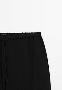 Mustat pellavahousut, joissa on joustava vyötärönauha ja kiristysnauha. Kangas on sileä ja malli on rento.