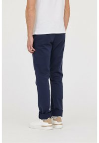 Pantalons en coton bleu marine à coupe fuselée, avec des poignets repliés, associés à des baskets blanches avec des accents beiges.