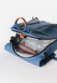 Zaino blu realizzato in materiale liscio con dettagli in pelle marrone. L'interno spazioso è caratterizzato da una fodera a motivo a griglia e scomparti per l'organizzazione.