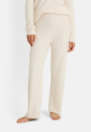 pantalones de descanso de tela peluda color crema con corte recto, que presentan una textura suave y bajos remallados, mostrados con pies descalzos.