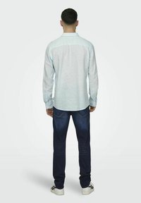 Lichtblauwe overhemd met lange mouwen en een button-down kraag, gedragen met donkerblauwe jeans en witte sneakers, gezien vanaf de achterkant.