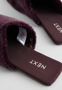 Purple faux fur slippers with a flat sole, featuring a smooth fabric insole and the brand name "NEXT" printed in white on the footbed.