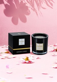 Bougie parfumée en verre noir avec des accents dorés, présentée à côté d'une boîte noire étiquetée "Gisada IRIS". Des pétales environnants ajoutent de la douceur à la scène.