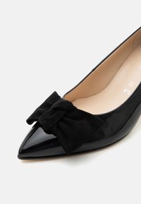 Chaussure plate en cuir verni noir à bout pointu avec un grand nœud noir doux à l’avant et une doublure intérieure beige.