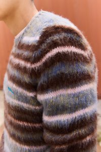 Pruhovaný pletený svetr v hnědé, růžové a modré barvě. Měkká, nadýchaná textura s kulatým výstřihem. Výrazné horizontální pruhy a vyšívané detaily.