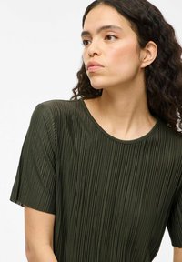 Top plissettato verde scuro, con maniche corte e scollatura tondeggiante. Realizzato in tessuto testurizzato, presenta pieghe verticali per un tocco di dettaglio in più.