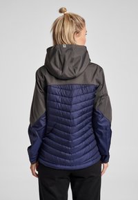 Vadderad jacka med huva; har en grå övre del och en marinblå nedre del med horisontella sömmar. Mjuk textur, praktisk design.