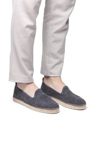 Grijze canvas espadrilles met een golvend textuur, slip-on ontwerp en jute zool. Gepaarde met lichte, taps toelopende broeken.