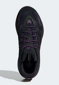 Black athletic shoe with mesh and suede materials, featuring purple accents, textured lines, and patterned laces. Rounded toe and padded collar.