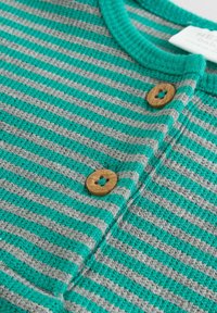 Grön- och grårandig textil med en strukturerad väv. Har träknappar. Rundad halsringning med grön kant.