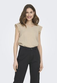 Haut beige avec décolleté en V et manches ornées de dentelle, associé à un pantalon cargo noir avec poches latérales. Tissu lisse avec une coupe décontractée.