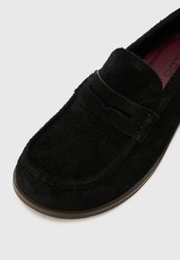 Musta daimista slip-on -kengät, joissa on pehmeä rakenne, pyöreä kärki, koristeelliset ompeleet ja hillitty kohotettu yksityiskohta varren yli.