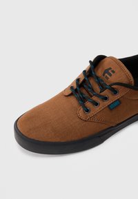 Pruunist kanvasest tennisetooted musta tallaga ja mustade paeltega, millel on sinised aktsendid, ning seljal väike "etnies" silt ja logo.