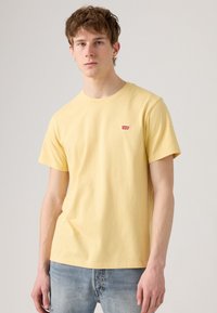 Camiseta de algodón de manga corta de color amarillo con cuello redondo, que cuenta con un pequeño logo rojo de Levi's en el lado izquierdo del pecho.