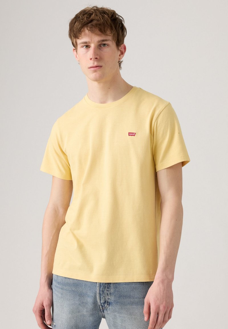 Camiseta de algodón de manga corta de color amarillo con cuello redondo, que cuenta con un pequeño logo rojo de Levi's en el lado izquierdo del pecho.