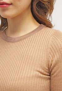 Beżowy sweter o prążkowanej fakturze z okrągłym dekoltem, z kontrastowym prążkowanym akcentem przy kołnierzu i teksturalnym wykończeniem na całej powierzchni.
