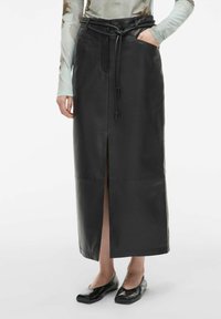 Crna kožna maksi suknja s visokim prorezom, remenom u struku i detaljima na džepovima. Materijal ima glatku teksturu i prilagođen kroj.