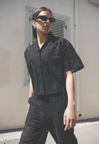 Ensemble coordonné en dentelle noire comprenant une chemise à col et manches courtes ainsi que des pantalons assortis avec une texture à motifs et une coupe décontractée.