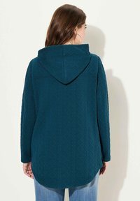 T:eal hoodie med texturerat diamantmönster, långa ärmar och en rymlig huva. Har en rundad nederkant och en avslappnad passform, i kombination med ljusa jeans.