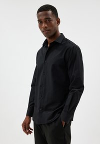 Camicia nera con colletto strutturato, maniche lunghe e tessuto testurizzato, caratterizzata da una vestibilità su misura e un leggero lucido.