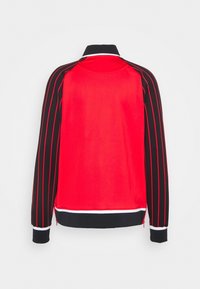 Chaqueta roja con mangas a rayas negras y rojas, cuello alto y acentos blancos. Textura suave, puños con cremallera y un diseño deportivo.