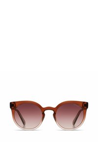 Ronde zonnebril met een amberkleurig frame, gradient roze lenzen en een subtiele cat-eye vorm. Transparant materiaal, minimalistische accenten.
