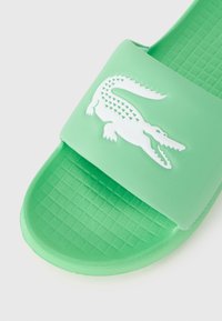 Green slide sandal with textured footbed and white embossed crocodile logo on the wide strap across the top.
