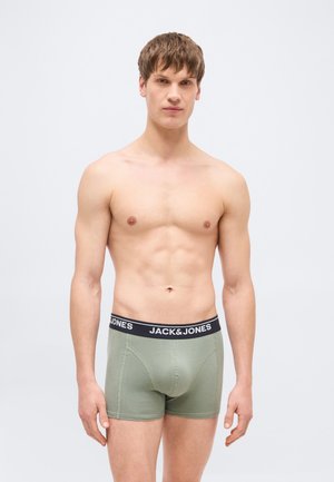 Junger Mann mit kurzen braunen Haaren, der helle grüne Boxershorts von Jack & Jones trägt und vor einem einfarbigen hellen Hintergrund steht.