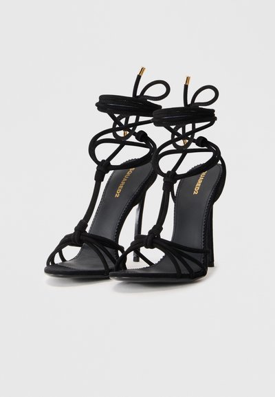 Svarta högklackade sandaler i mocka med en intrikat knutdesign, öppen tå och smal klack med guldaccenter.