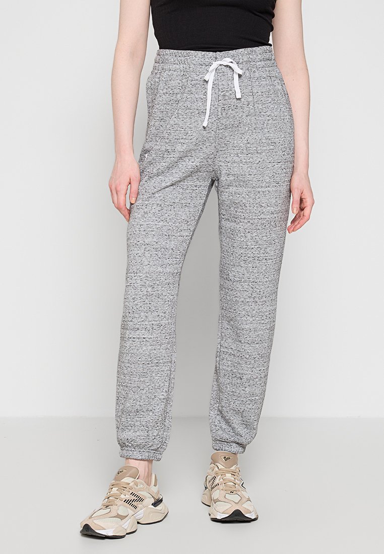 Pantalons de survêtement gris avec une finition texturée, taille élastique, cordon de serrage blanc et chevilles ajustées, associés à des chaussures de sport beiges.