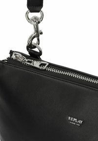 Borsa a tracolla in pelle nera con accessori in argento, dotata di chiusura con zip e etichetta con logo. Il manico ha un gancio staccabile per una maggiore versatilità.