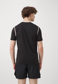 Camiseta atlética negra de manga corta con acentos de color claro en los hombros, textura suave y diseño de cuello redondo.