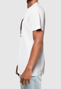 Bílý bavlněný tričko s krátkými rukávy, s grafickým designem na přední straně. Uvolněný střih a plochý výstřih. Lehce hladká textura.