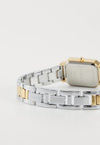 Stříbrné a zlaté kovové náramkové hodinky s obdélníkovým pouzdrem, designem spojovacího náramku a leštěným povrchem, s minimalistickým zadním víkem.